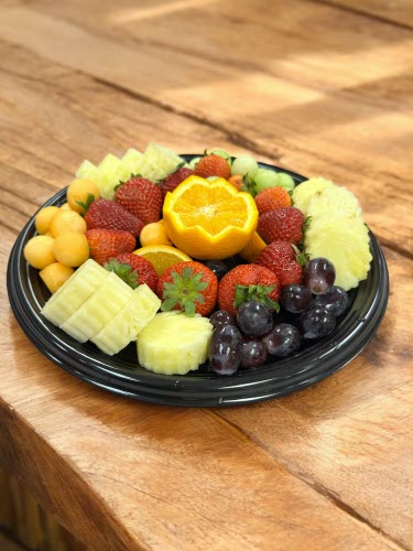 tray of fresh fruit, oranges, grapes, melon, pineapple and strawberries on a wooden counter