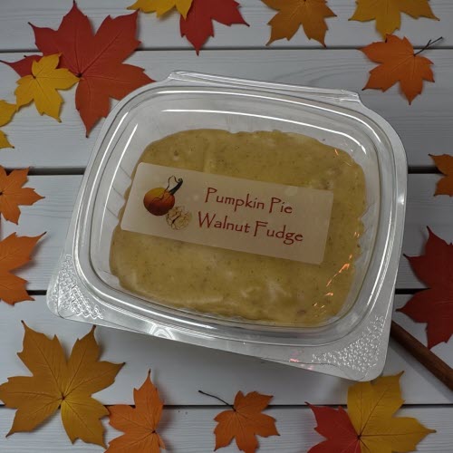 container of pumpkin pie walnut fudge on white washed wooden counter surrounded by maple leaves and cinnamon stick