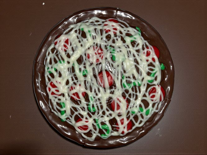 Milk chocolate personal pan potato chip pizza with red "pepperoni" and green "peppers" on a brown countertop